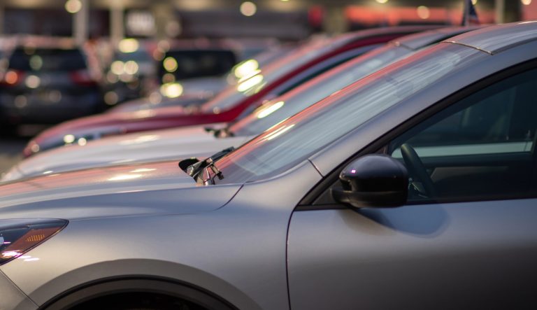 Rząd samochodów zaparkowanych na parkingu, widok z boku, wieczorne światła.