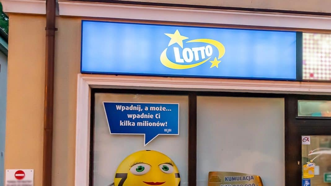 Sklep z logo Lotto i plakatem z uśmiechniętą twarzą, zachęcający do gry w loterię.