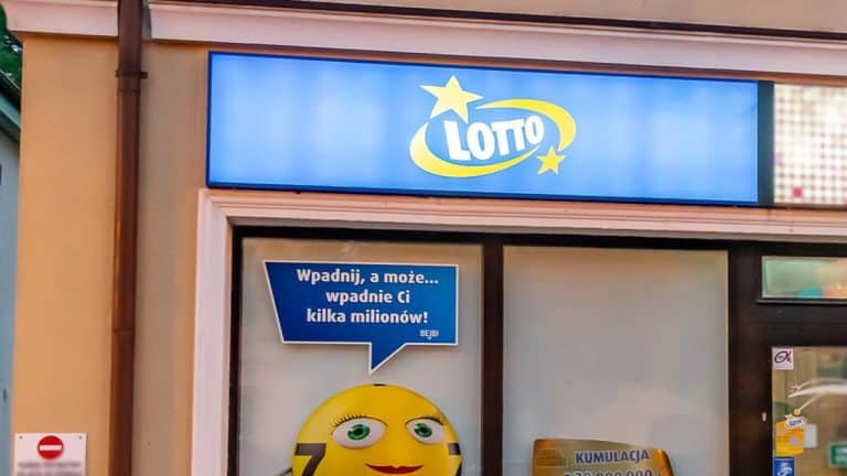Sklep z logo Lotto i plakatem z uśmiechniętą twarzą, zachęcający do gry w loterię.