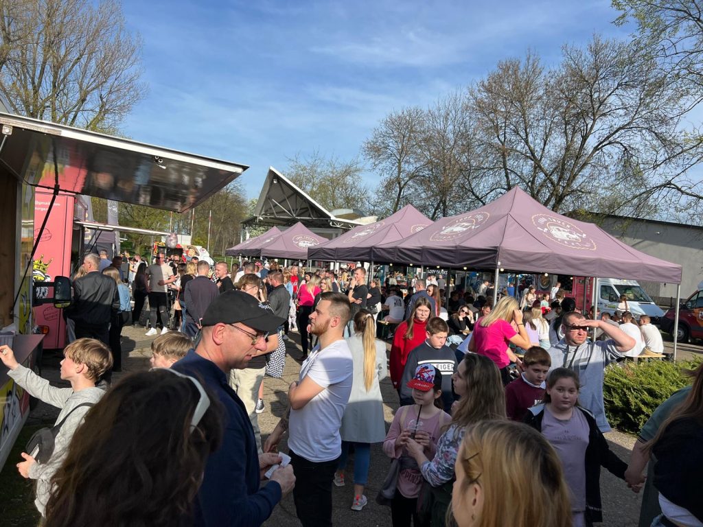 Tłum ludzi na festiwalu z namiotami i food truckami w tle, w słoneczny dzień.