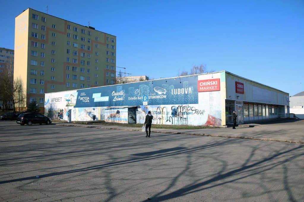 Budynek handlowy przy Hali Urania w Olsztynie, na ścianach graffiti, w tle blok mieszkalny.