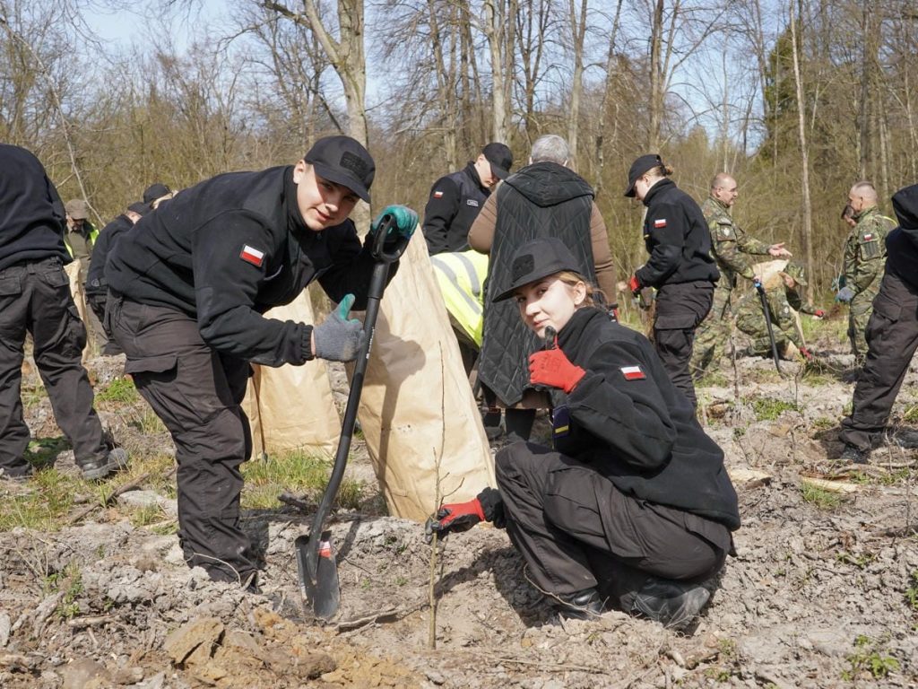 Grupa młodzieży i służb sadzi drzewa w lesie na Mazurach podczas akcji z okazji Światowego Dnia Ziemi.