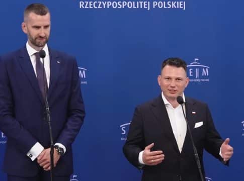 Dw&oacute;ch mężczyzn w garniturach podczas debaty w studiu z niebieskim tłem z napisem SEJM.