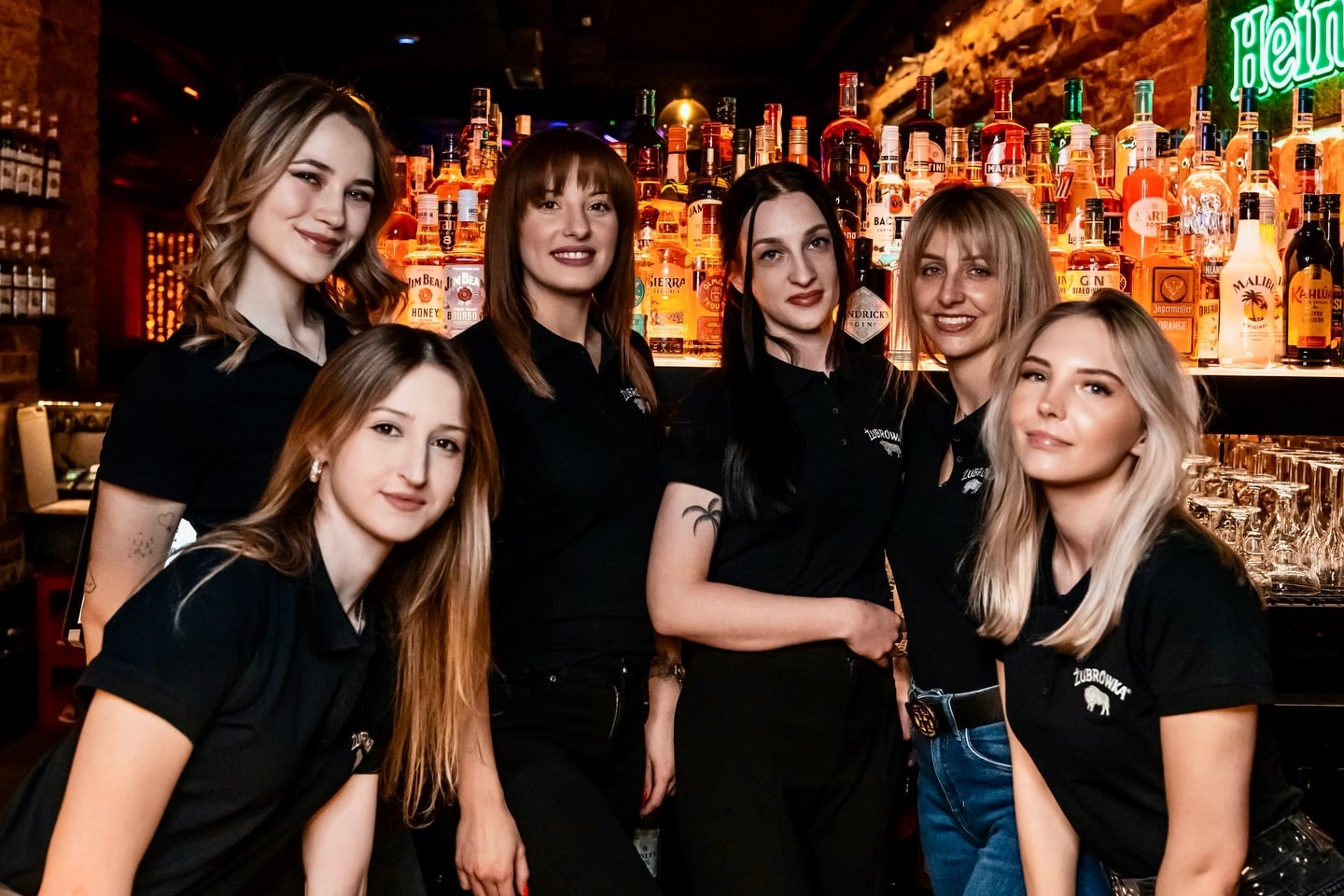 Grupa kobiet stojących za barem w nowym klubie na star&oacute;wce Olsztyna, w tle kolorowe butelki alkoholu.