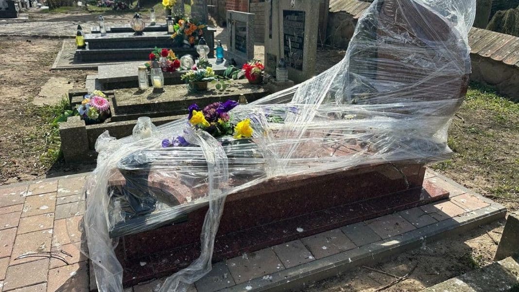 Nagrobek owinięty folią na cmentarzu w Jezioranach, wok&oacute;ł kwiaty i znicze.