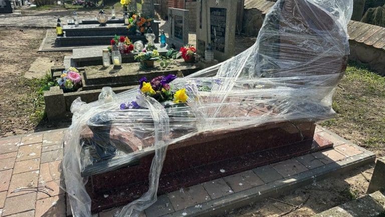 Nagrobek owinięty folią na cmentarzu w Jezioranach, wok&oacute;ł kwiaty i znicze.