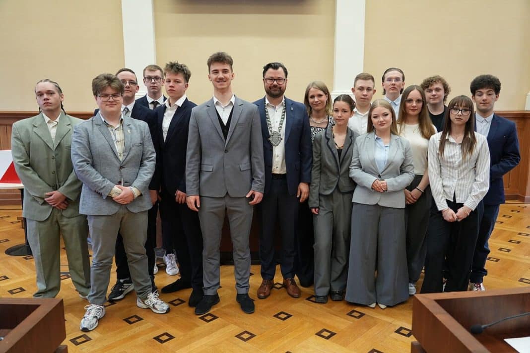 Grupa młodych radnych i władz miasta podczas oficjalnej sesji w sali konferencyjnej.