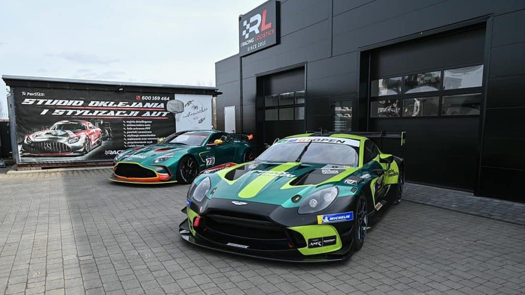 Dwa wyścigowe Aston Martiny GT3 i GT4 na podolsztyńskim parkingu, przygotowywane do start&oacute;w.