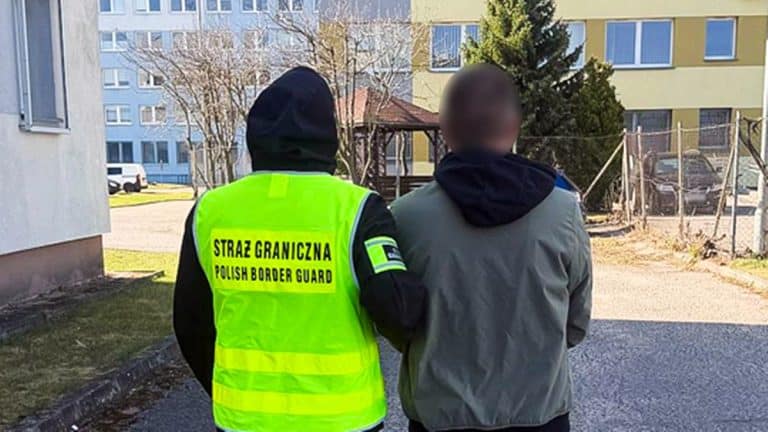 Funkcjonariusz Straży Granicznej i zatrzymany mężczyzna na ulicy, w tle budynki mieszkalne.