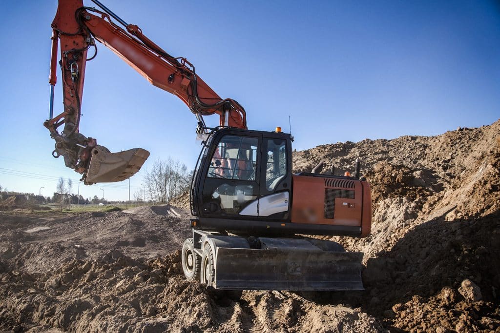 Koparka na placu budowy z dużą ilością ziemi i skał, pod niebem bez chmur.