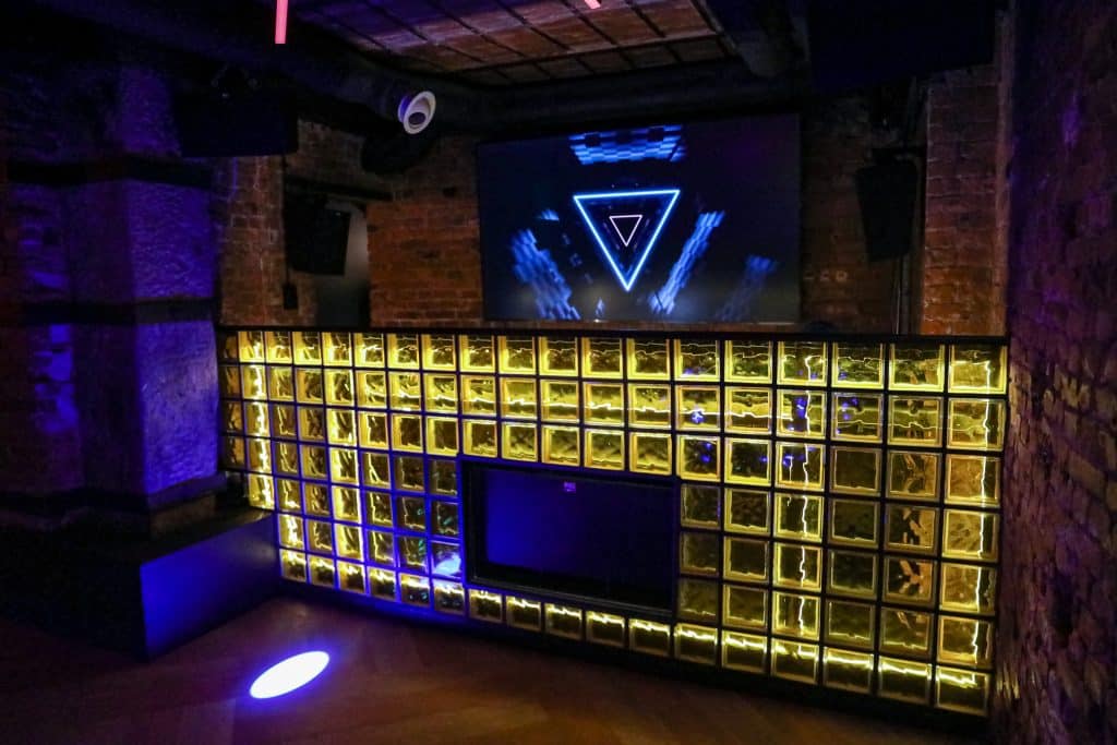 Wnętrze klubu Dyskoteka Music Bar w Olsztynie z podświetlonymi elementami i dużym ekranem.