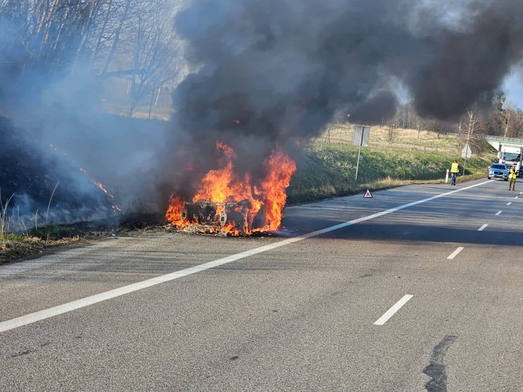 Samoch&oacute;d marki Audi płonie na drodze ekspresowej S22, w pobliżu Braniewa, z widocznymi służbami na miejscu.