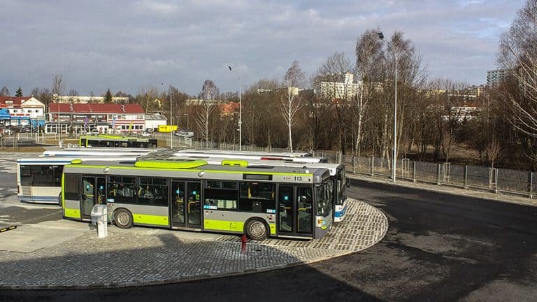 Nowoczesny autobus na pętli autobusowej z widokiem na miasto i drzewa w tle.