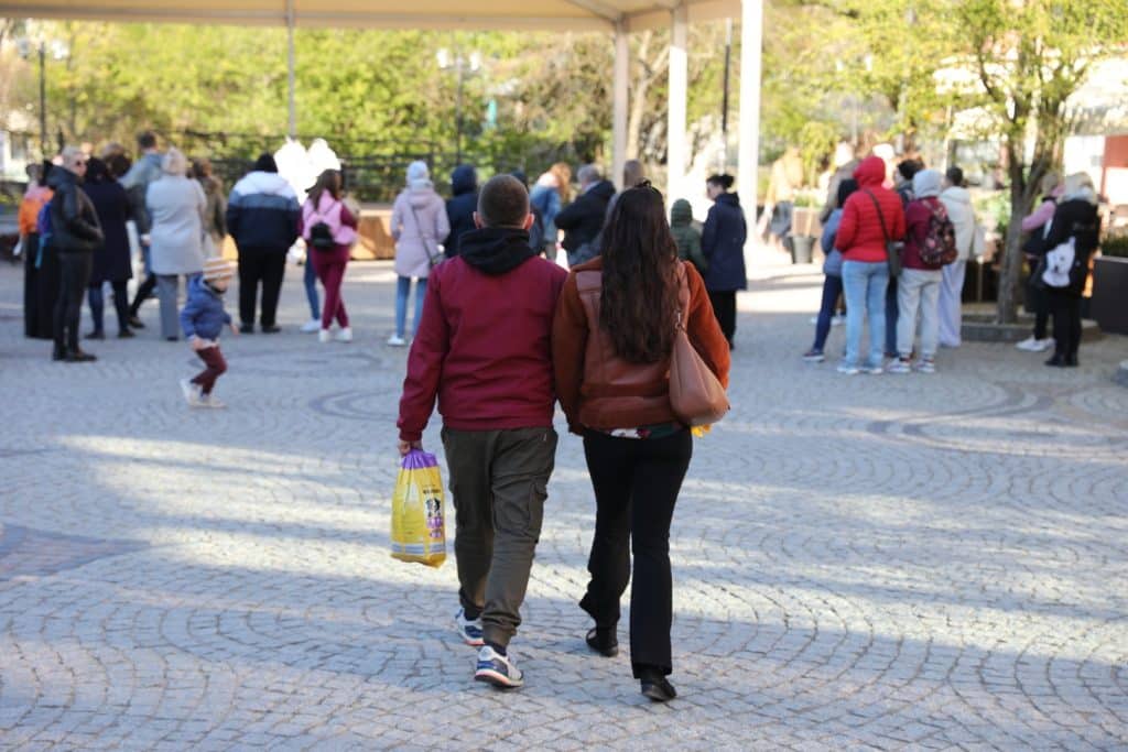 Grupa ludzi na Targu Rybny w Olsztynie podczas wydarzenia upamiętniającego Łukasza Litewkę, z uczestnikami przynoszącymi karmę dla zwierząt.