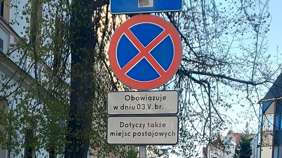 Znak zakazu zatrzymywania się na tle drzew i budynk&oacute;w w centrum miasta.