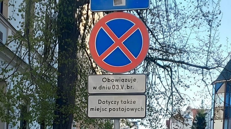 Znak zakazu zatrzymywania się na tle drzew i budynk&oacute;w w centrum miasta.