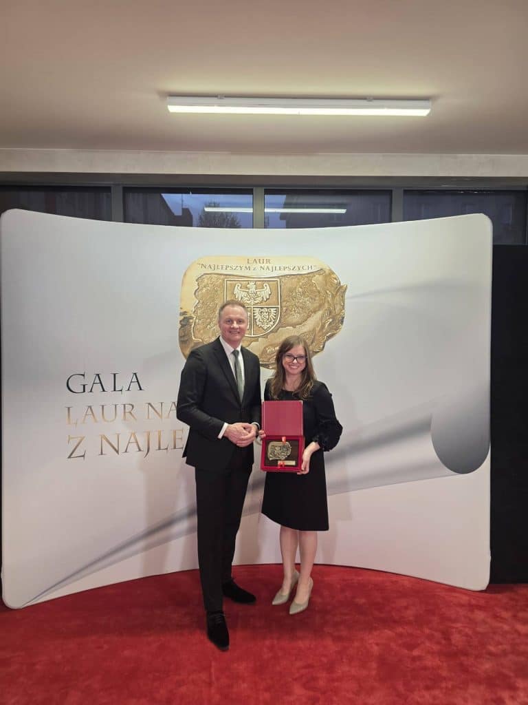 Zdjęcie przedstawia kobietę i mężczyznę na gali, kobieta trzyma medal w ozdobnym pudełku, oboje uśmiechnięci.