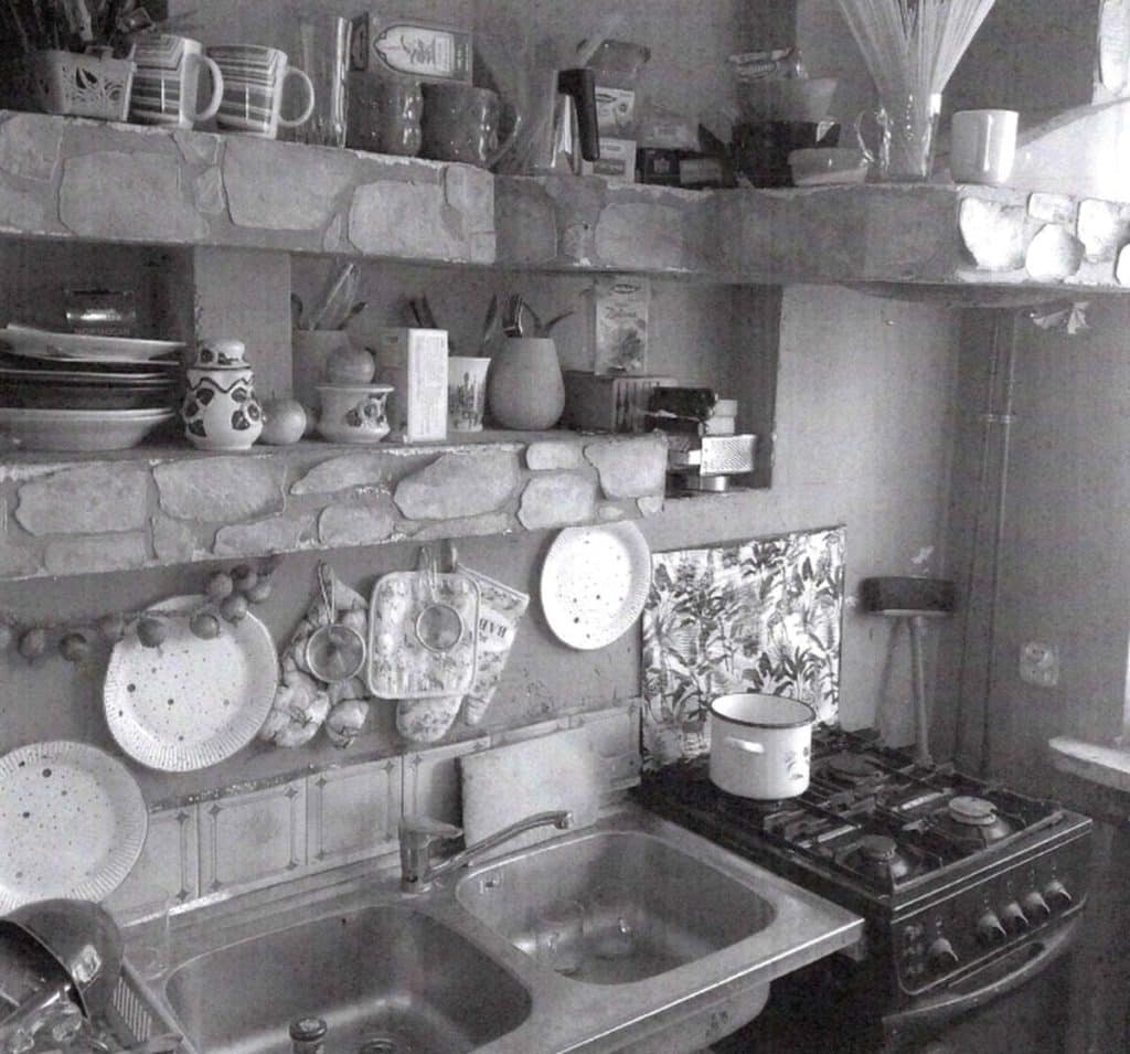 Wnętrze kuchni z widocznymi naczyniami i sprzętem, w czarno-białej tonacji.