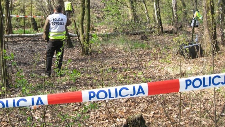 Policjant na miejscu zdarzenia w lesie, otoczonym taśmą policyjną, w Dobrym Mieście.