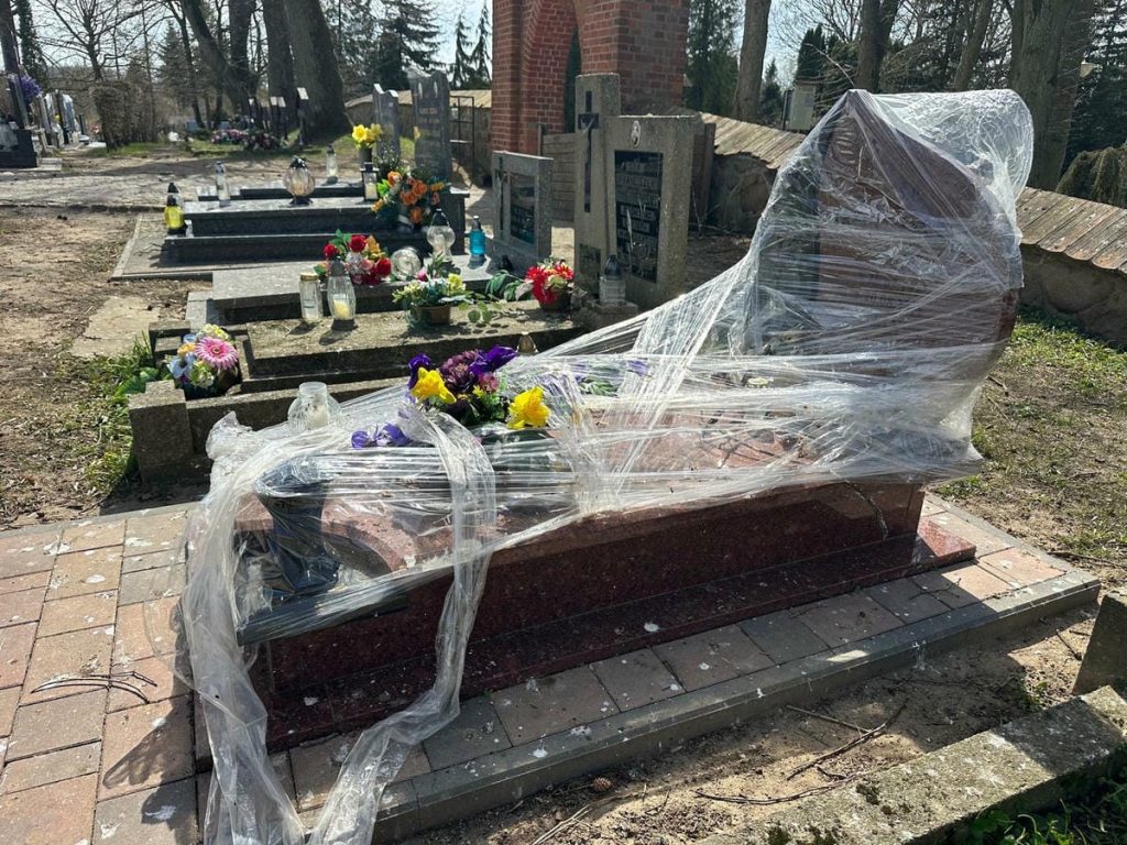Nagrobek owinięty folią na cmentarzu w Jezioranach, wok&oacute;ł kwiaty i znicze.