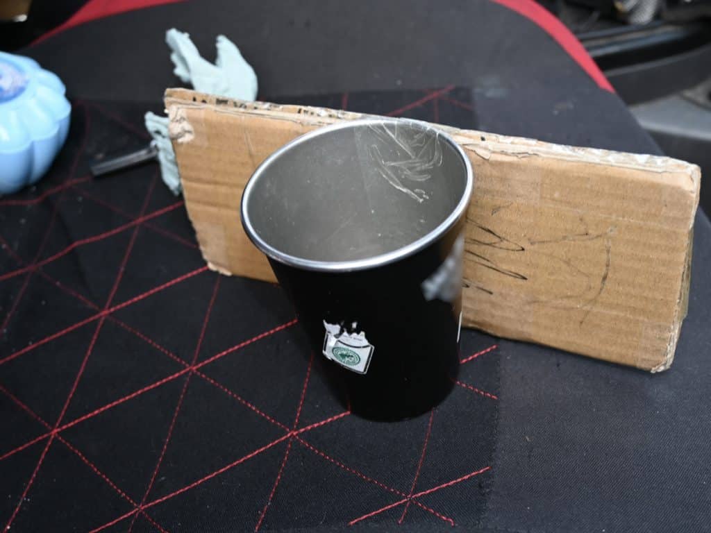 Pusty kubek i kawałek kartonu na czarnym tle, w tle fragment samochodu.