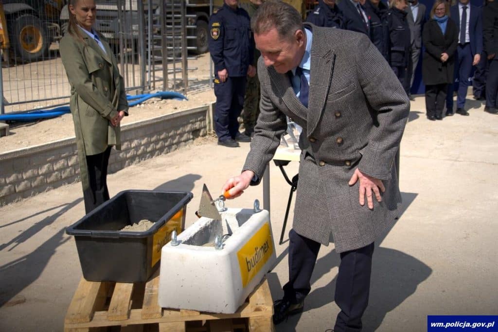 Mężczyzna w garniturze kładzie beton na placu budowy nowej komendy policji w Ostr&oacute;dzie.