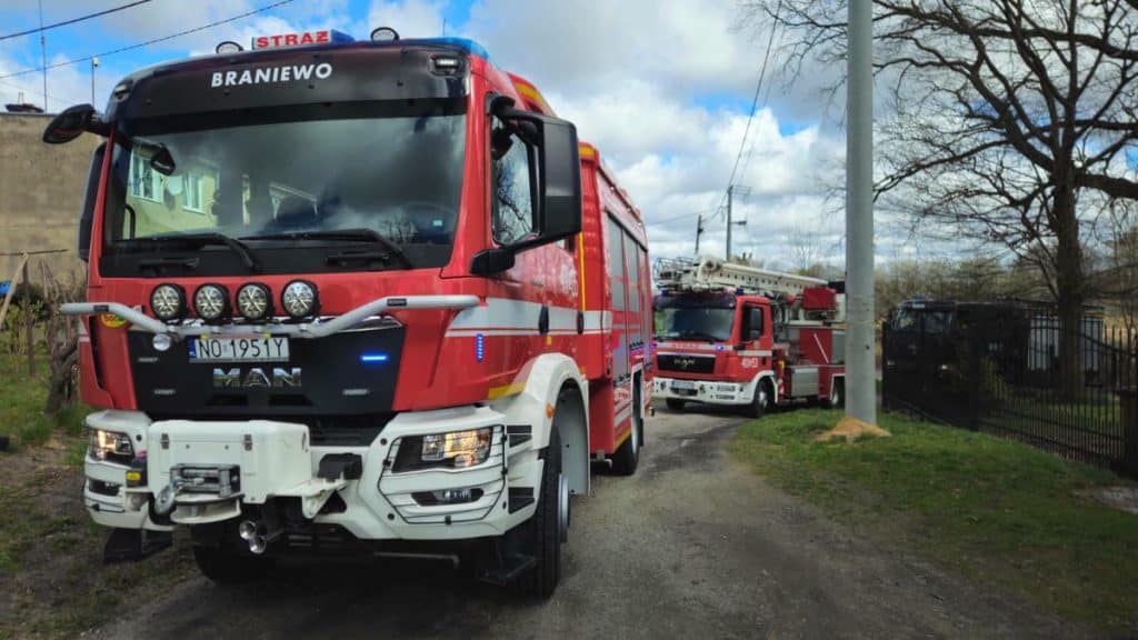 Dwa czerwone samochody straży pożarnej na ulicy, w tle drzewa i budynki.