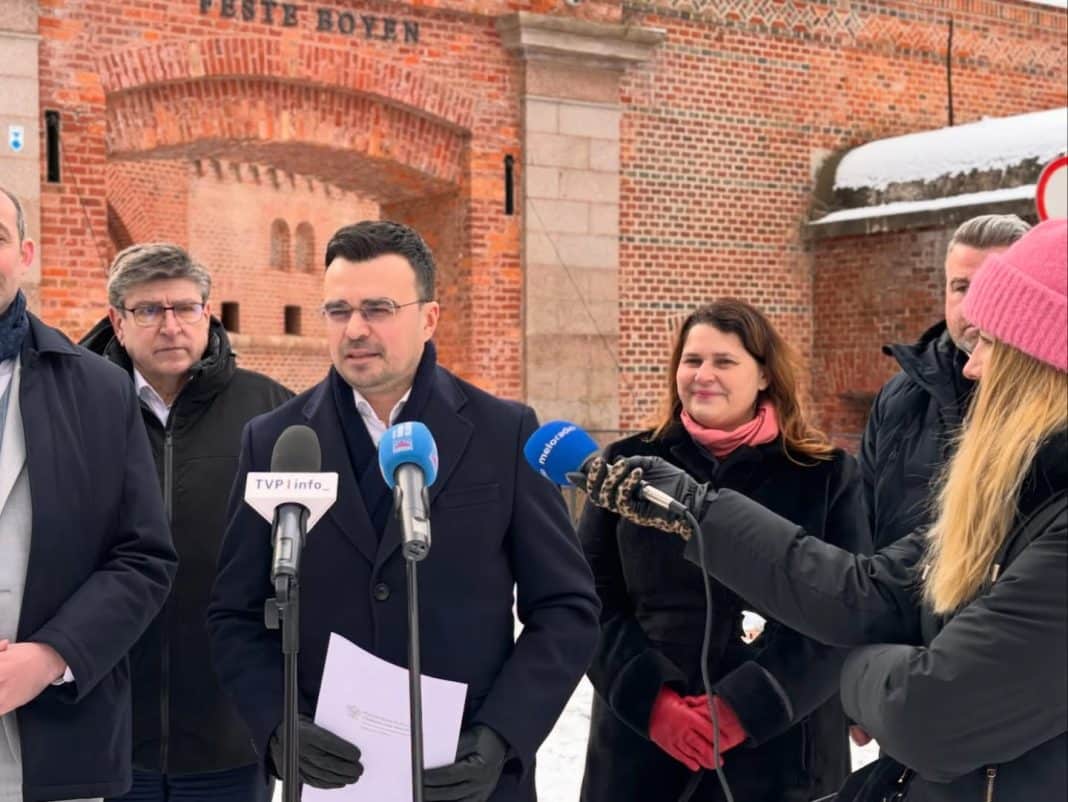 Grupa os&oacute;b podczas konferencji na tle zamku w Olsztynie, w zimowej scenerii.