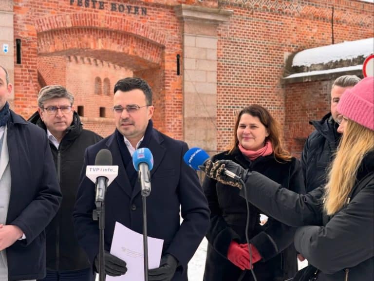 Grupa os&oacute;b podczas konferencji na tle zamku w Olsztynie, w zimowej scenerii.