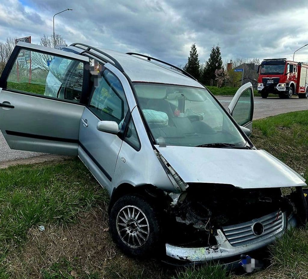 Rozbity samoch&oacute;d na poboczu z uszkodzonym przodem i otwartymi drzwiami.