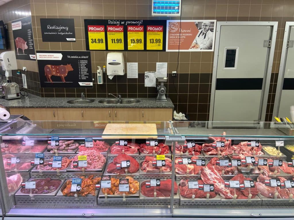 Mięso i wyroby mięsne w chłodnym stoisku sklepowym, widoczne ceny i oznaczenia.