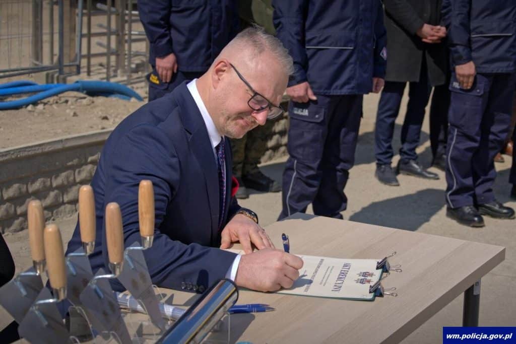 Mężczyzna podpisuje dokument podczas uroczystości rozpoczęcia budowy nowej komendy policji w Ostr&oacute;dzie.