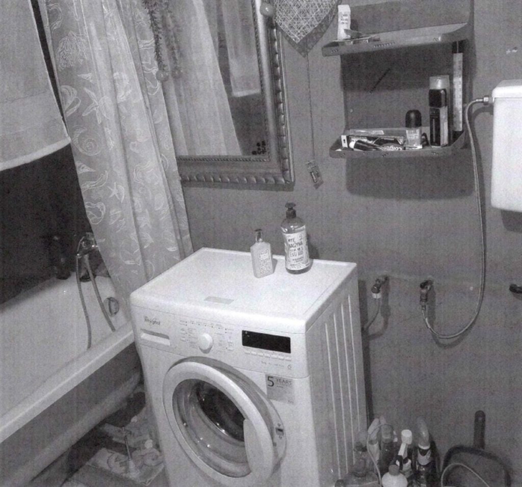 Wnętrze małej łazienki z pralką, lustrem, umywalką i r&oacute;żnymi przedmiotami na p&oacute;łkach.