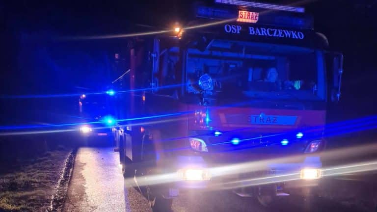 Samoch&oacute;d straży pożarnej na drodze nocą po wypadku, oświetlony niebieskimi światłami.