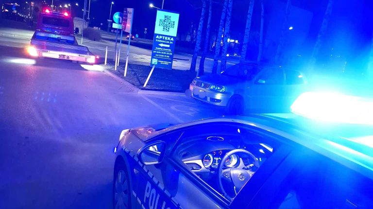 Zdjęcie policyjnego samochodu na tle innych pojazd&oacute;w podczas nocnej interwencji.