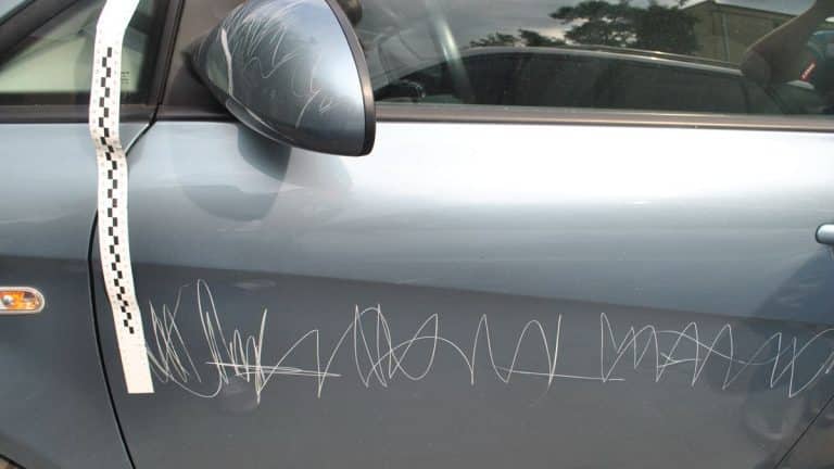 Samoch&oacute;d zarysowany ostrym narzędziem, widoczny na zdjęciu, z licznymi rysami na drzwiach.