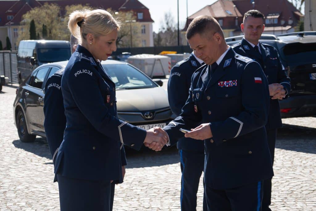 Policjanci podczas oficjalnej prezentacji nowych radiowoz&oacute;w na Mazurach, w tle samochody i budynki.