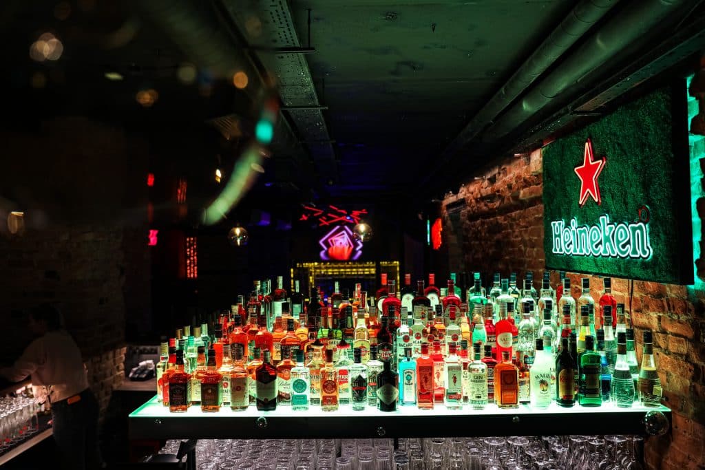 Widok na bar z szerokim wyborem alkoholi, neonowe oświetlenie i ceglane ściany w klubie Dyskoteka Music Bar w Olsztynie.