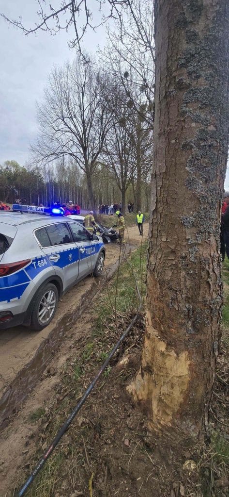Rozbity samoch&oacute;d na drzewie podczas rajdu, z udziałem służb ratunkowych i kibic&oacute;w na miejscu.