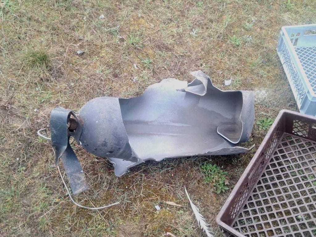 Zniszczony fragment samochodu dostawczego po wybuchu na drodze S7, leżący na trawie obok koszy na śmieci.