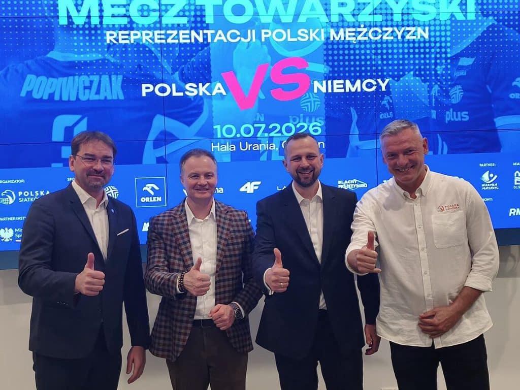 Czterech mężczyzn na tle ekranu z informacją o meczu Polska-Niemcy, uśmiechnięci i pokazujący gesty thumbs up.