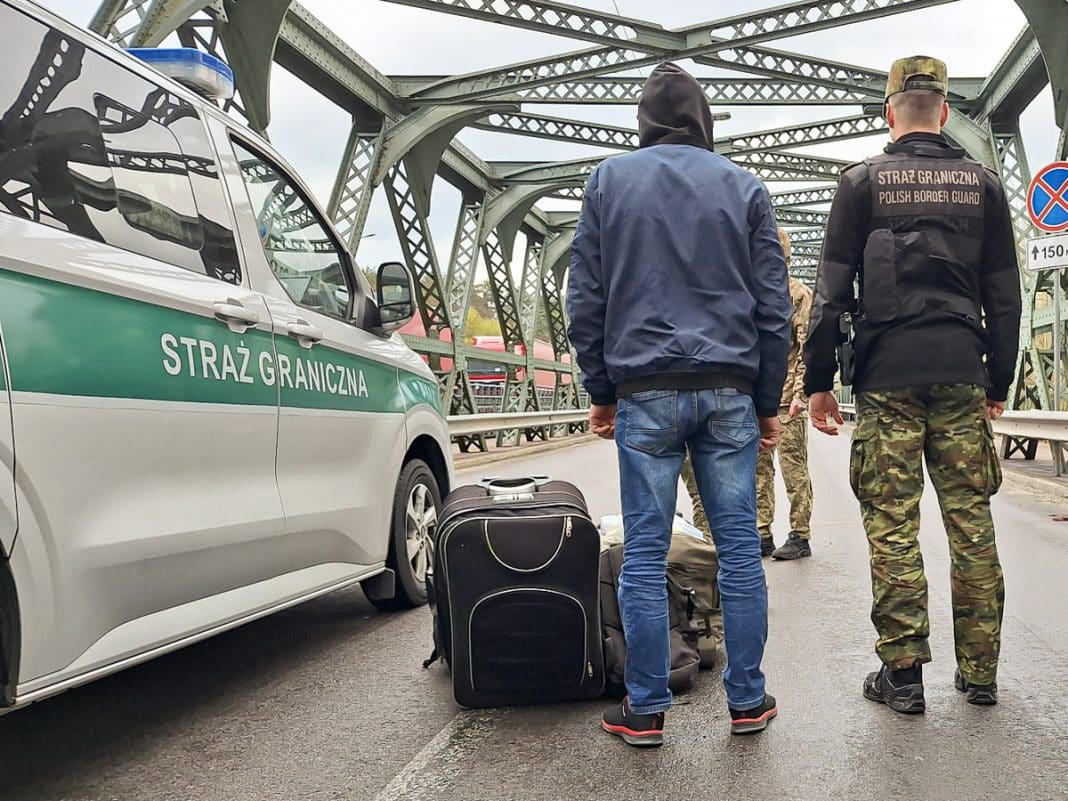 Funkcjonariusze Straży Granicznej zatrzymują cudzoziemc&oacute;w na moście, obok walizek i samochodu służbowego.