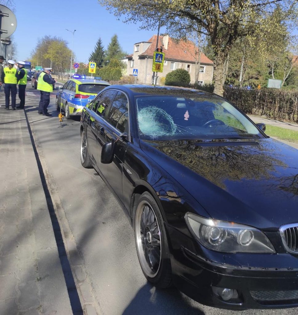 Wypadek na przejściu dla pieszych, uszkodzony samoch&oacute;d i policjanci na miejscu zdarzenia.