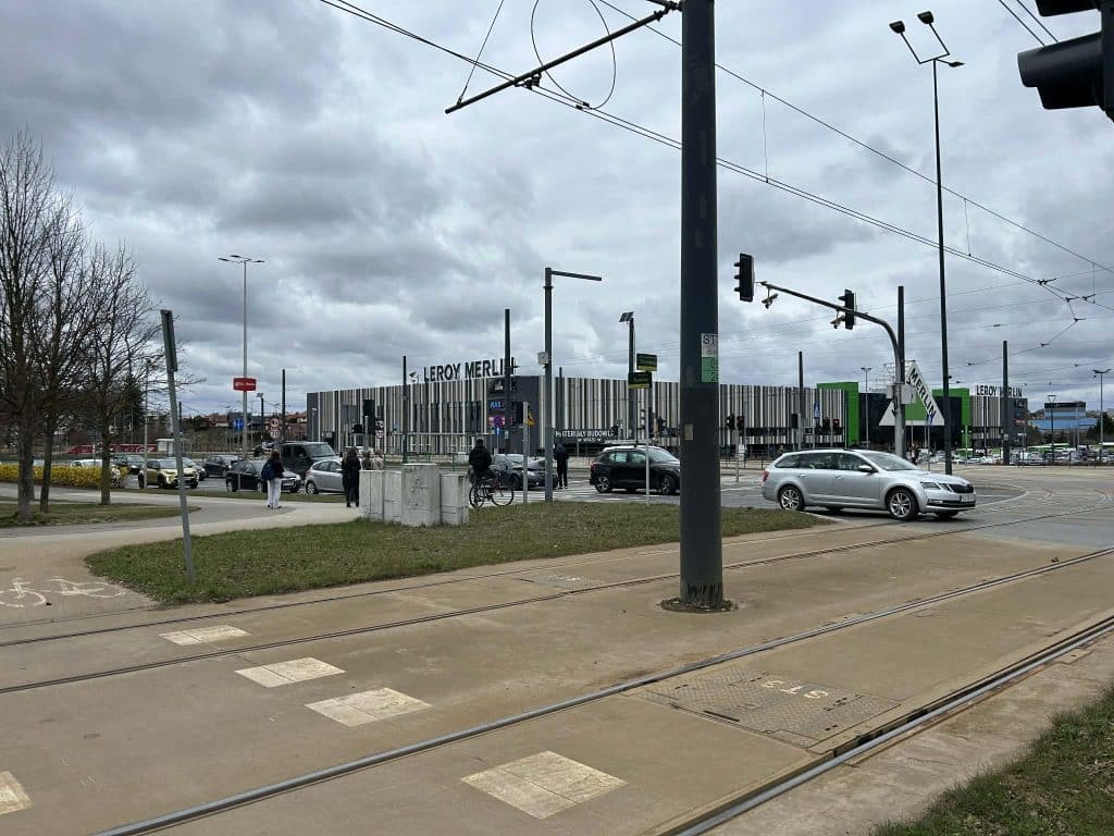 Zdjęcie z zatłoczonego skrzyżowania przy Galerii Warmińskiej, z samochodami i pieszymi, w tle sklep Leroy Merlin.