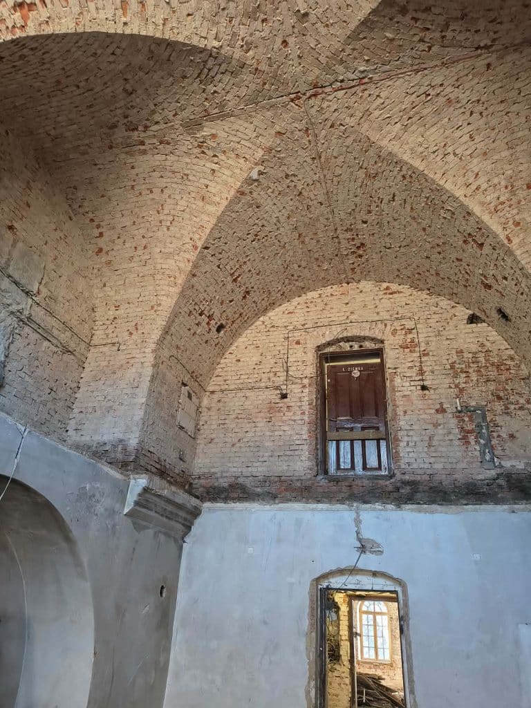 Wnętrze zabytkowej ceglanej architektury w trakcie remontu, widoczne łuki i okna.