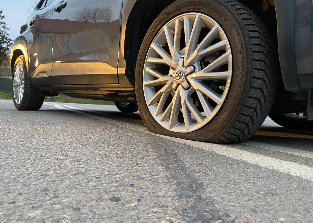 Zdjęcie samochodu z przebitym kołem na drodze, widoczny detal opony i felgi.