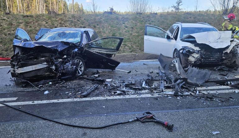 Rozbity samoch&oacute;d na drodze po zderzeniu, służby ratunkowe na miejscu.