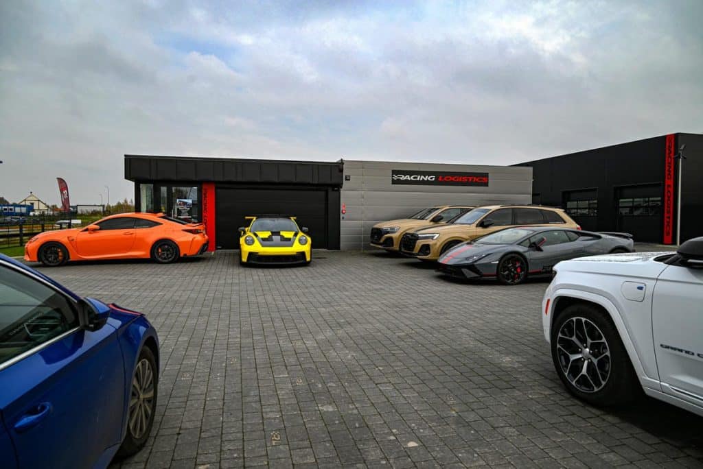 Na parkingu pod Olsztynem stoją wyścigowe Aston Martiny GT3 i GT4, obok inne luksusowe samochody.