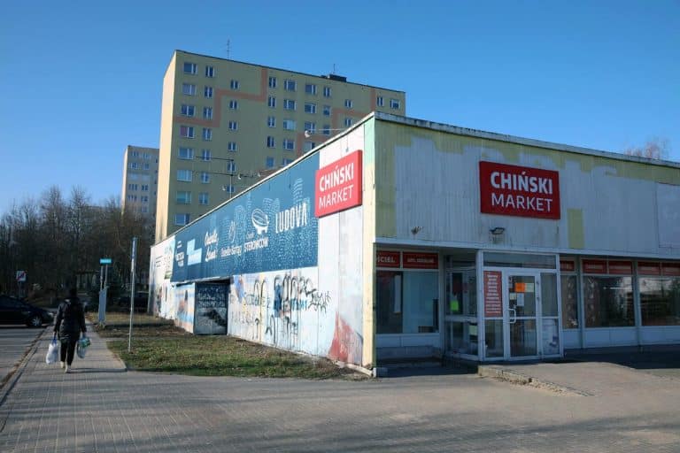Budynek handlowy przy Hali Urania w Olsztynie, z widocznym napisem 'Chiński Market', w tle wysokie bloki mieszkalne.