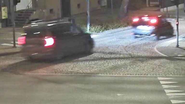 Zdjęcie z policyjnej interwencji, dwa samochody na ulicy w nocy, jeden z nich odjeżdża, w tle oświetlone budynki.